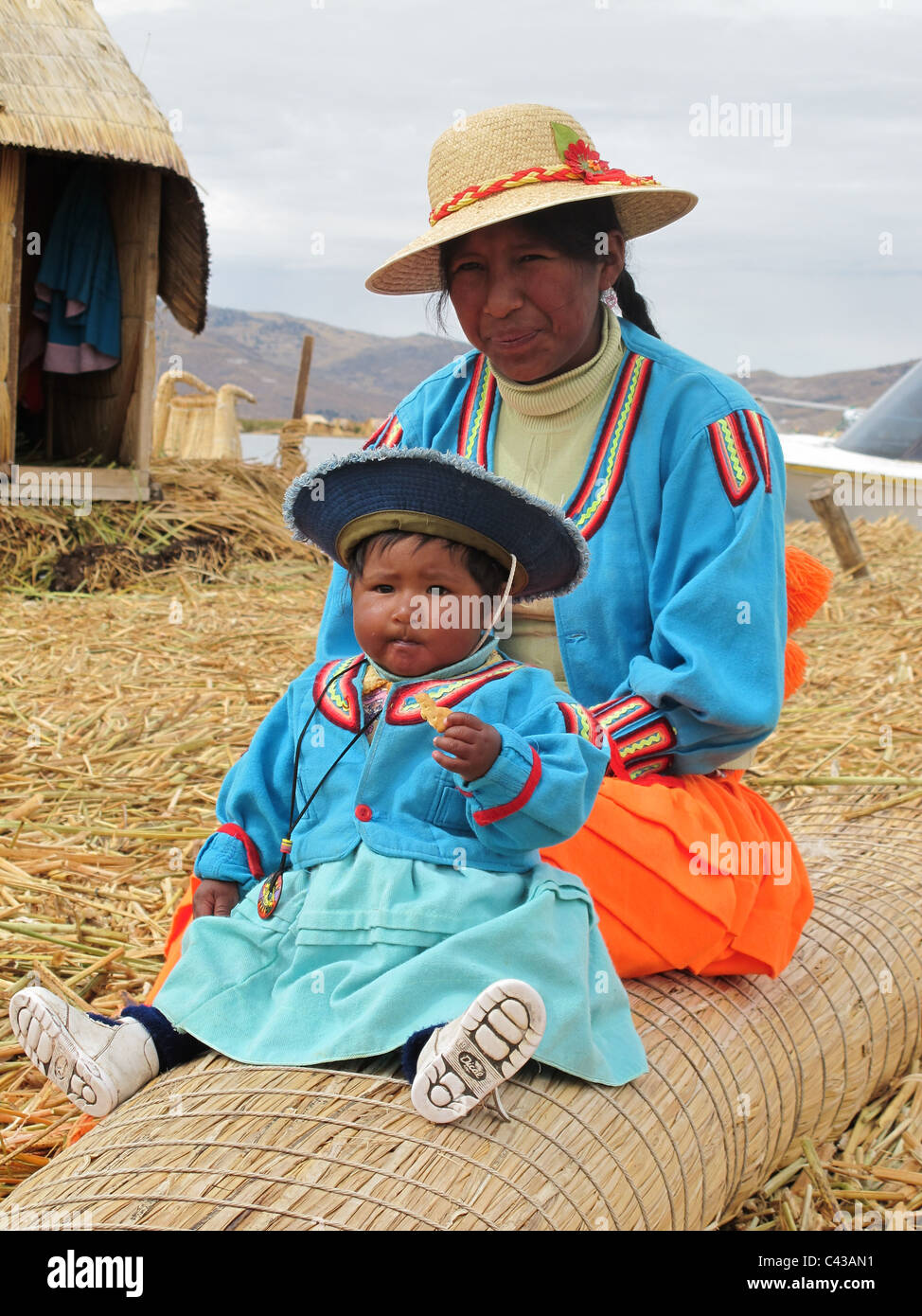 Uro mother and child traditionally dressed sitting on a reed bench in front of their reed house on the floating island Stock Photo