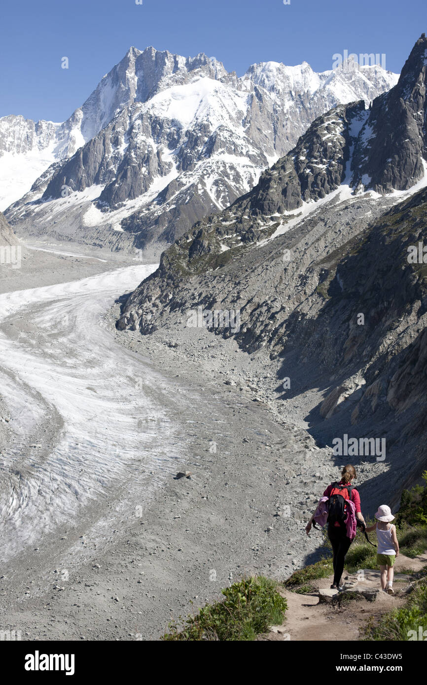 Young lady and a child hiking on a trail overlooking "Mer de Glace" in the Mont Blanc Massif. The far mountains are the Grandes Jorasses. France. Stock Photo