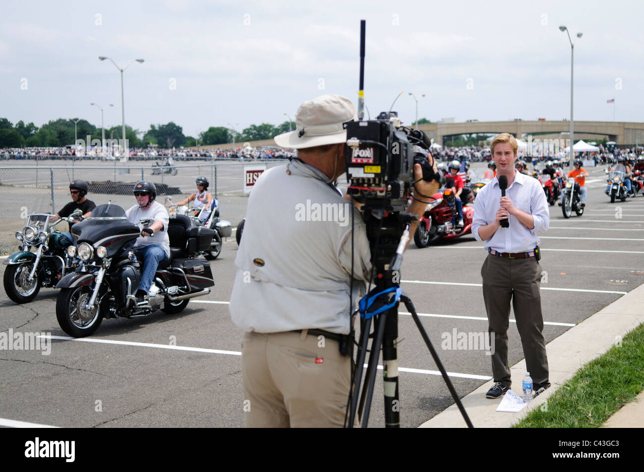 ARLINGTON, VA - A TV reporter broadcasts a feed in front of the riders departing for the annual Rolling Thunder motorcycle rally through downtown Washington DC on May 29, 2011. This shot was taken as the riders were leaving the staging area in the Pentagon's north parking lot, where thousands of bikes and riders had gathered. Stock Photo