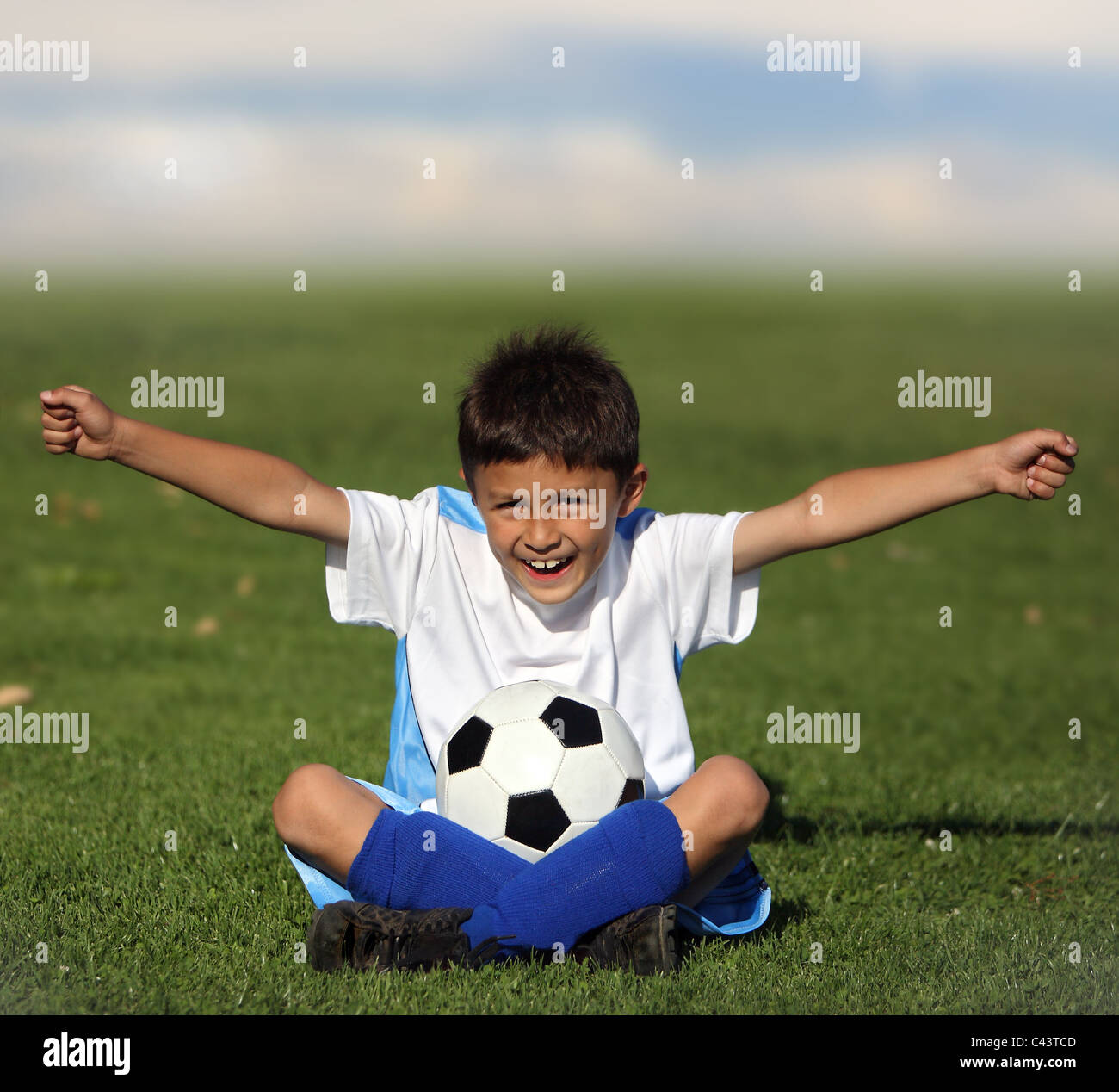 Boy sitting in field with arms out with soccer ball Stock Photo