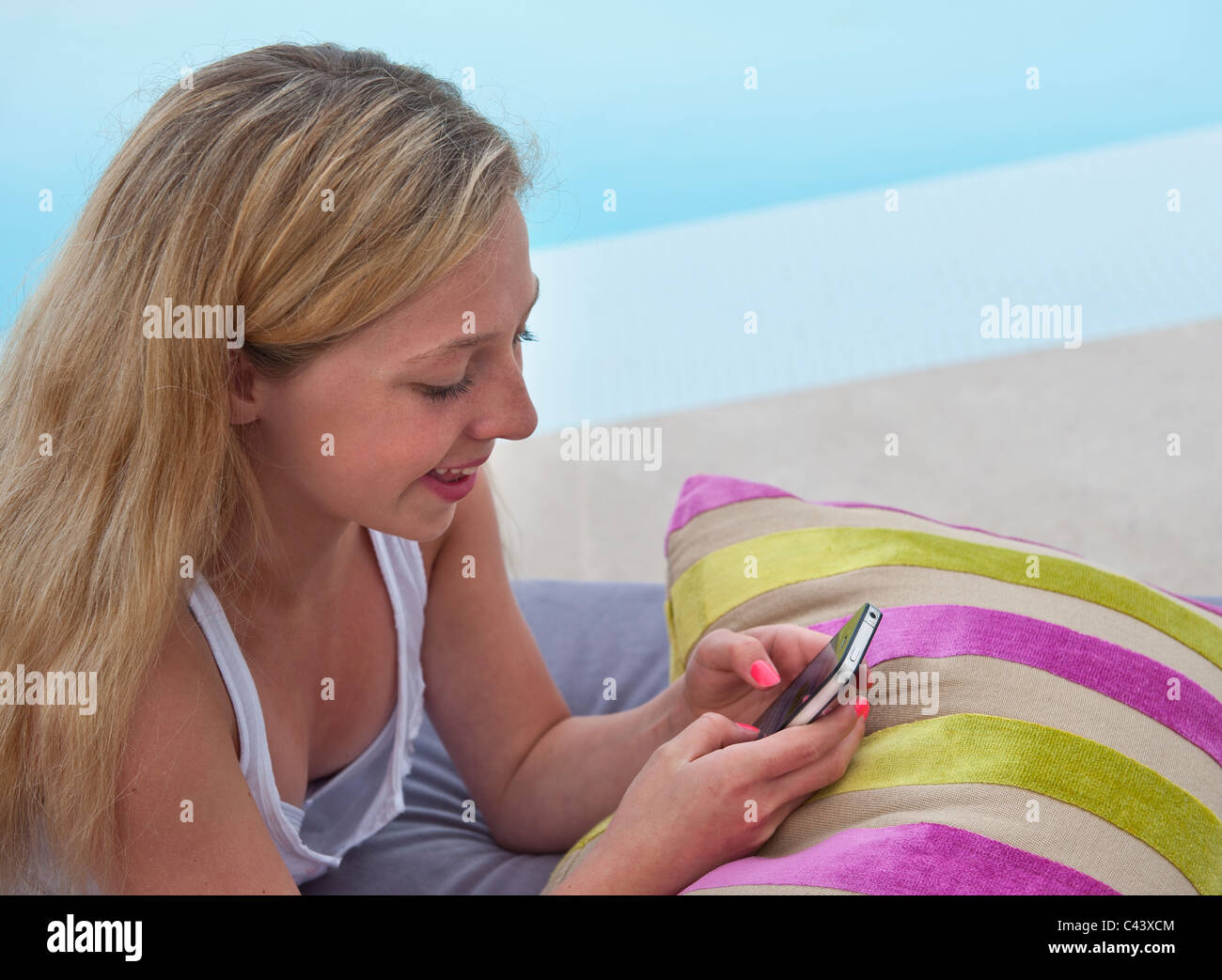 TEEN TEXTING FACEBOOK APP attractive 13-15 years teenage blond girl, with smartphone in luxury holiday vacation setting texting & using social media Stock Photo