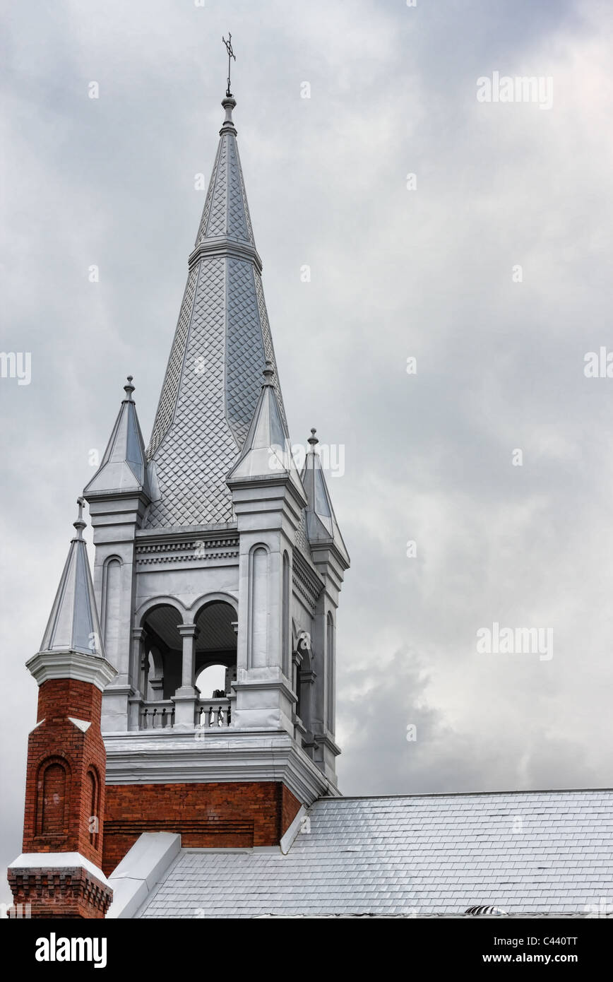 Church steeple with details of tiled roof materials and dramatic cloudy sky Stock Photo