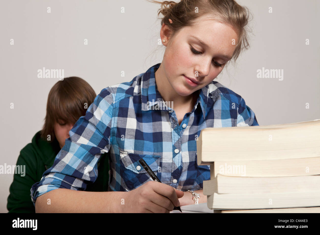 A teenage girl doing class work, boy in background Stock Photo