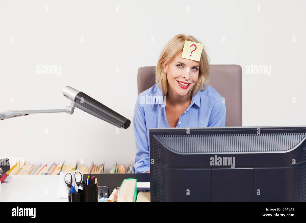 A woman sitting at an office desk with an adhesive note on her forehead Stock Photo