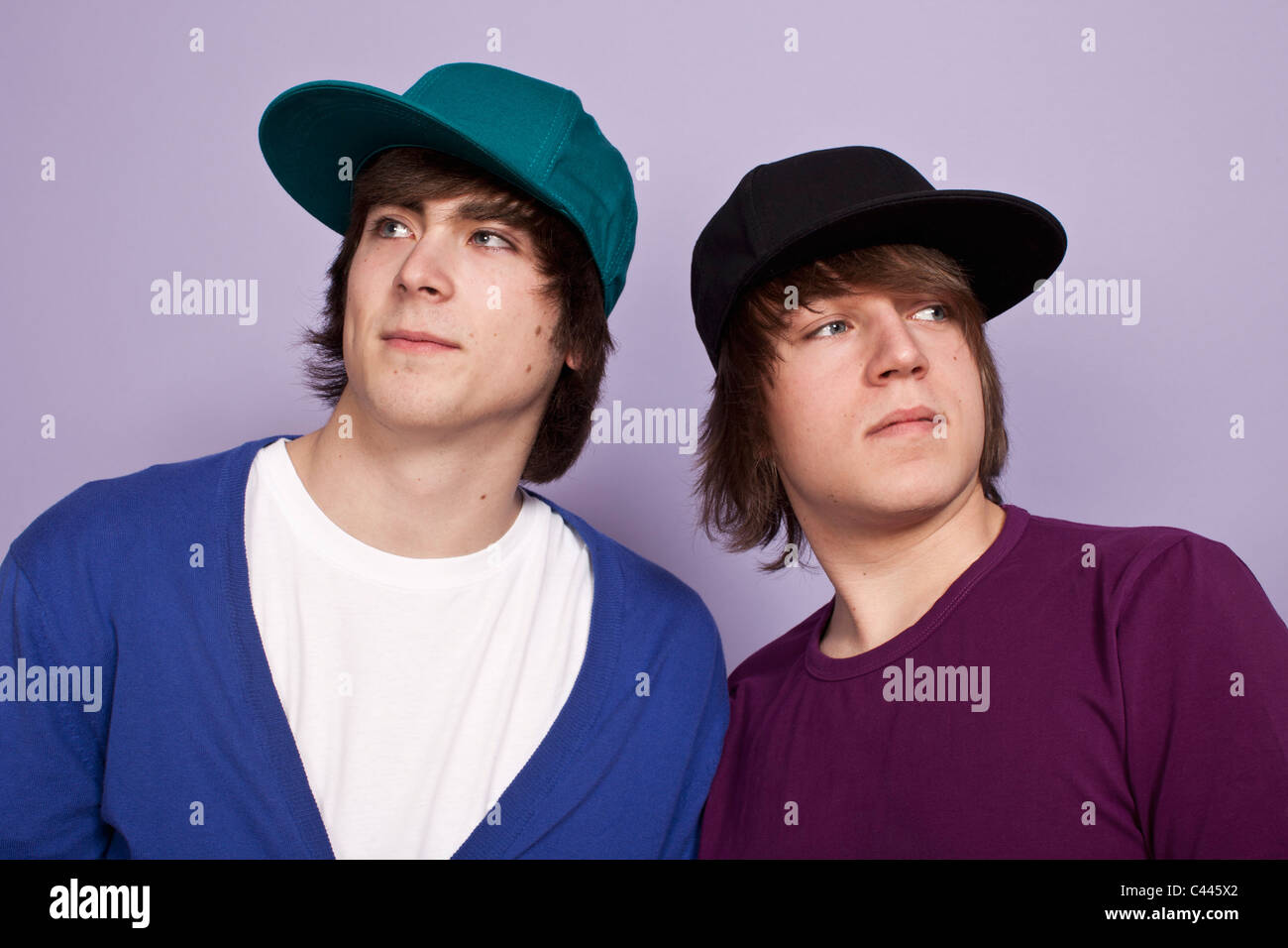 Two teenage boys wearing baseball caps looking away, studio shot Stock Photo