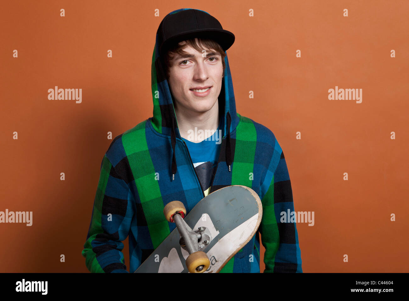 A teenage boy holding a skateboard, portrait, studio shot Stock Photo