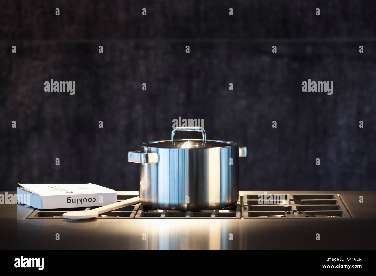 Saucepan, cookery book and wooden spoon on hob. Stock Photo