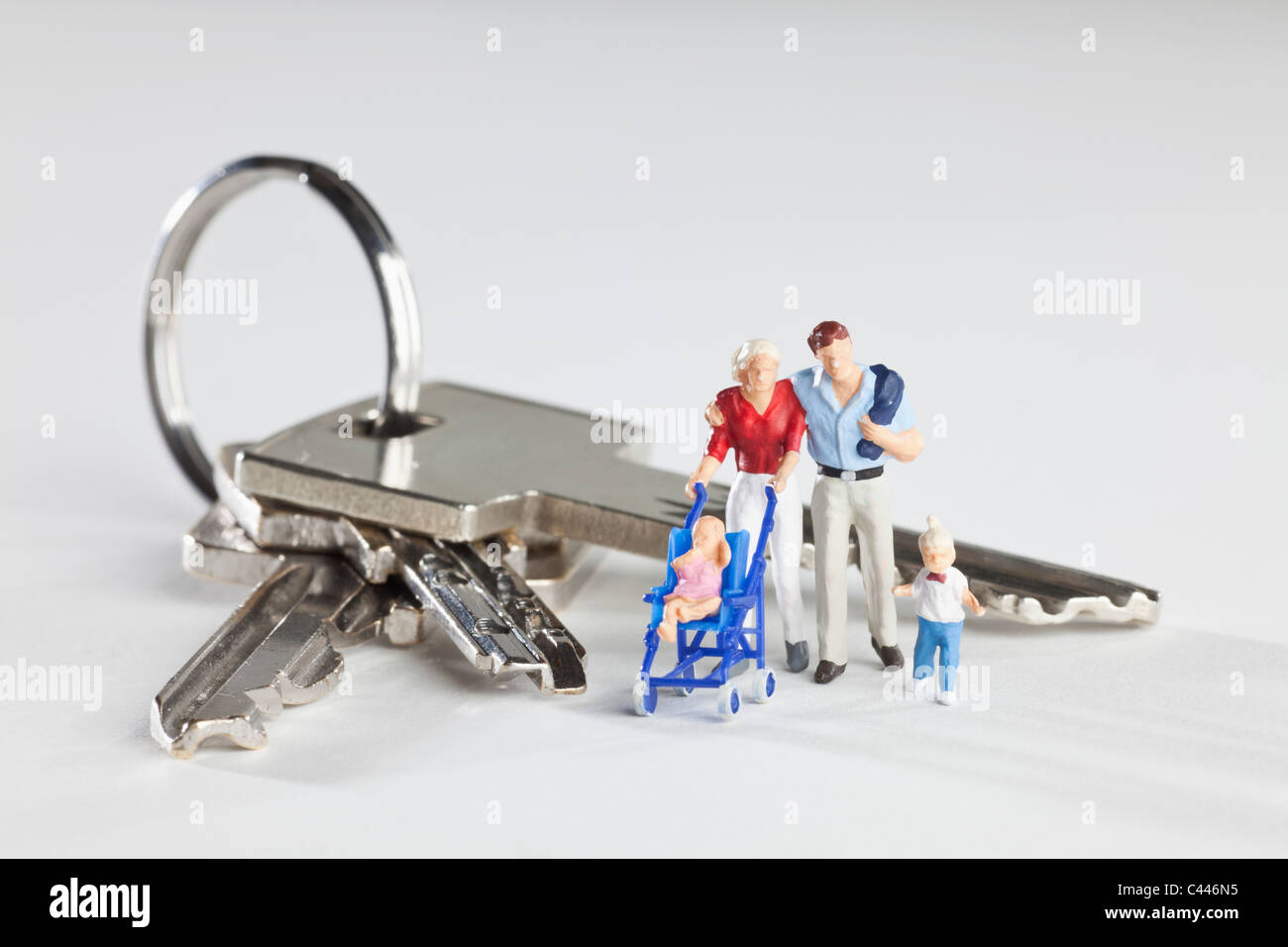 A young family of miniature figurines standing next to house keys on a key ring Stock Photo