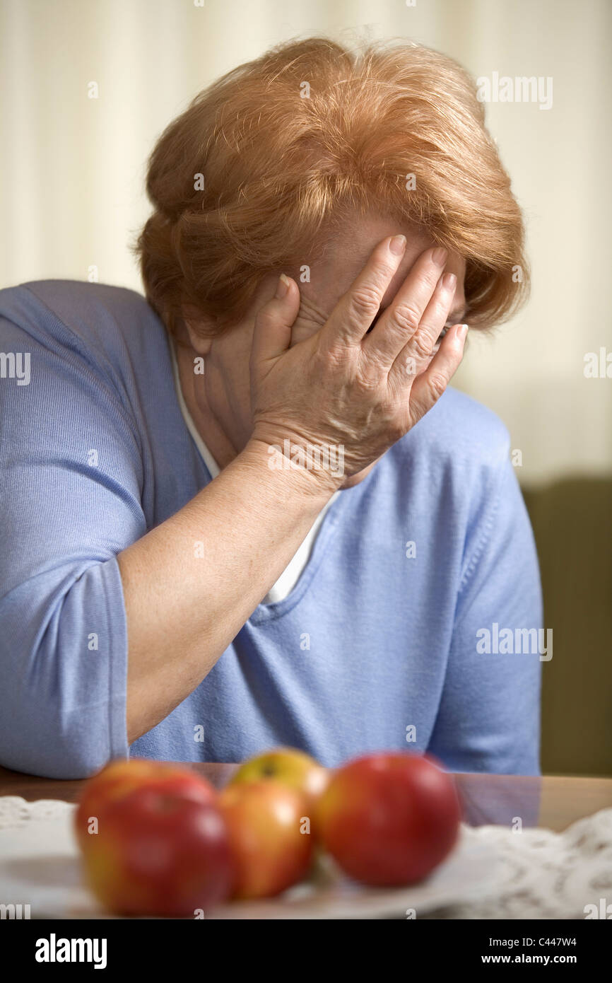 A senior woman sitting at a table covering her face with her hand Stock Photo