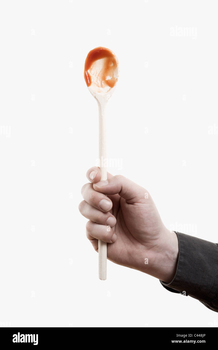 A man holding aloft a wooden spoon with red sauce on it Stock Photo