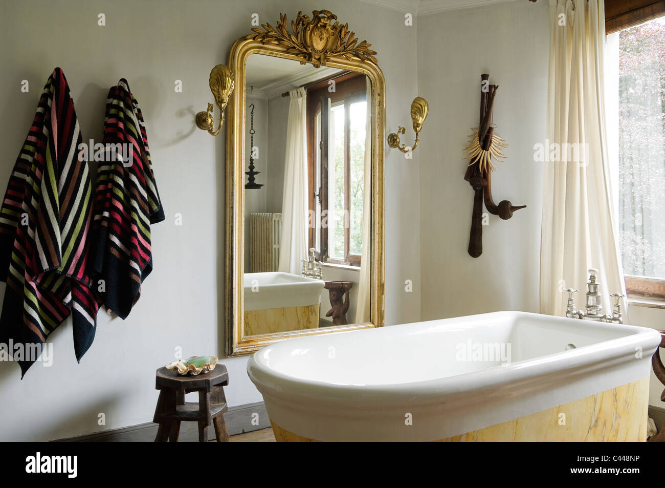 Freestanding marble bathtub in bathroom with wooden flooring and large gilt framed mirror Stock Photo