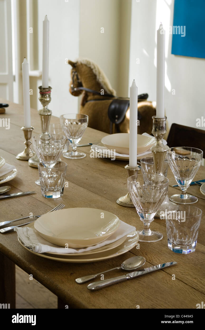 Wooden dining table laid with place setting, candles and glassware. A