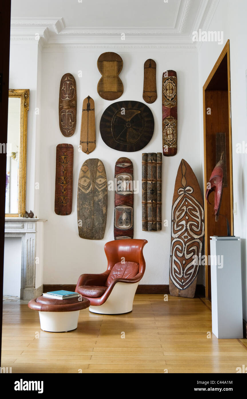 A collection of African tribal shields displayed on a wall in room with oceanic war shield and danish leather chair Stock Photo