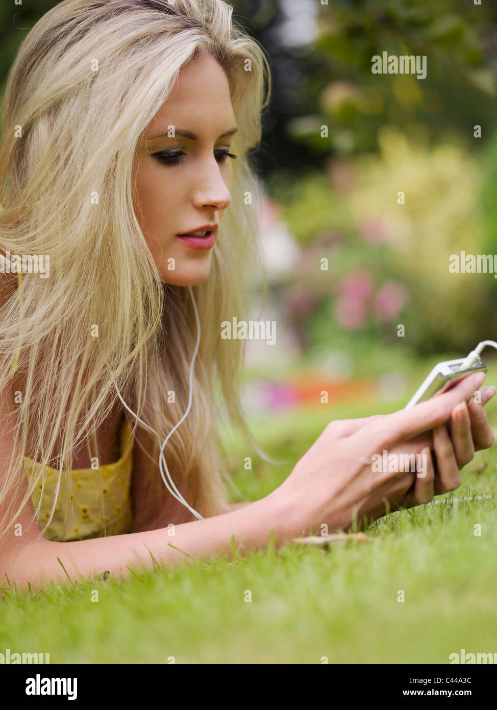 A woman lying in the grass listening to an MP3 player Stock Photo - Alamy