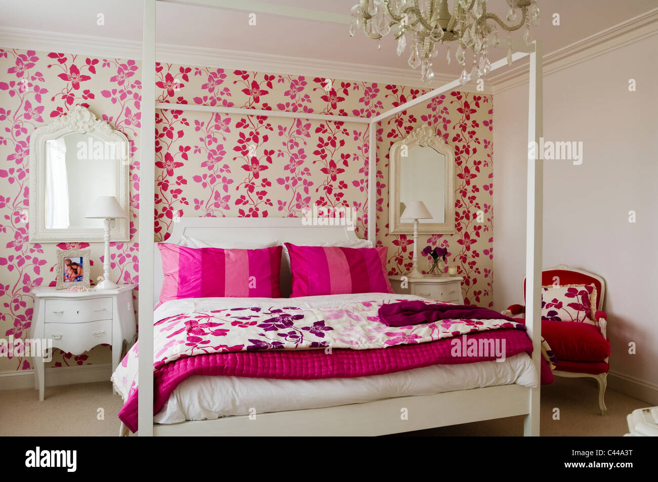 White fourposter bed in bedroom with Designer's Guild pink floral patterned wallpaper and chandelier Stock Photo