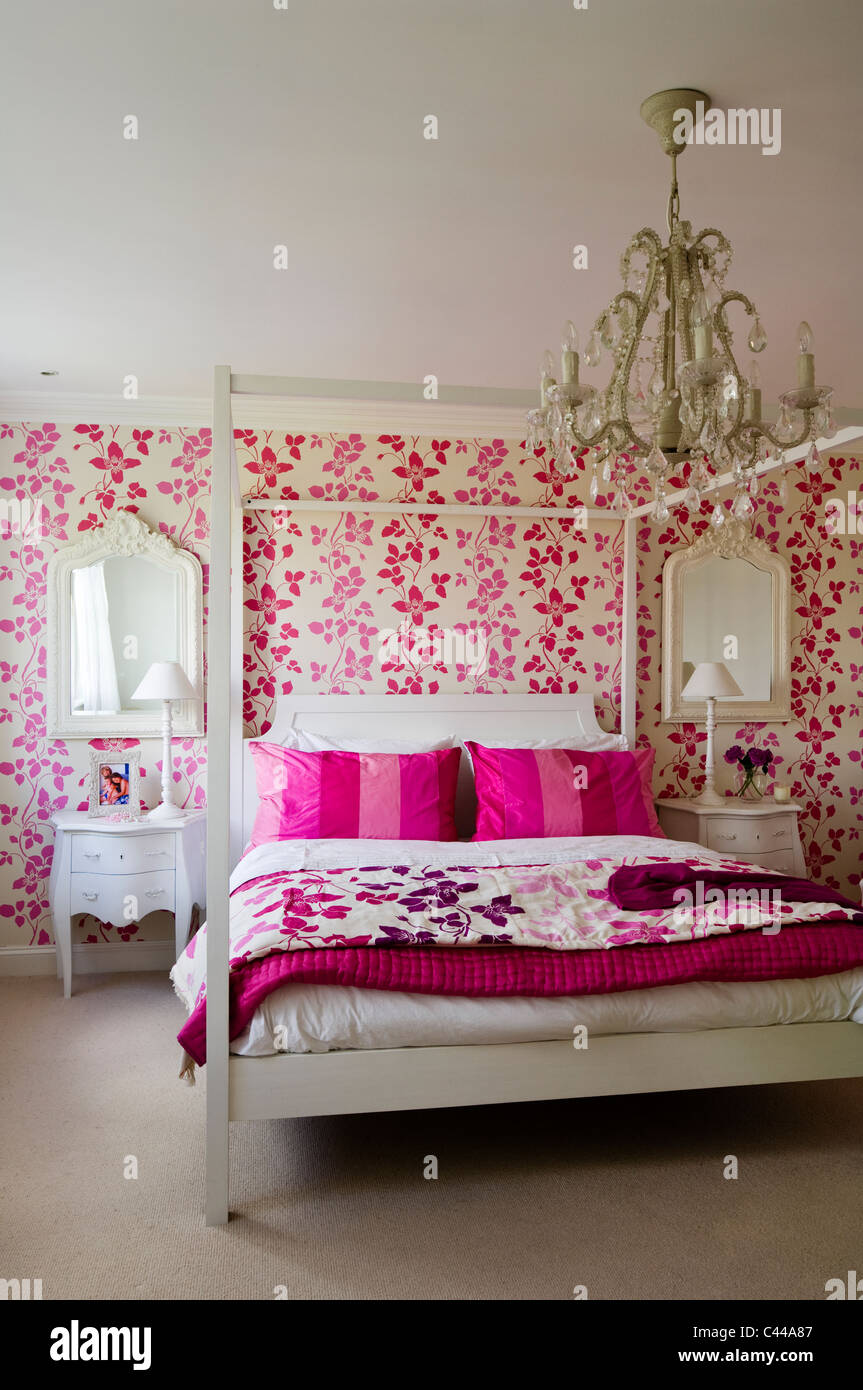 White fourposter bed in bedroom with Designer's Guild pink floral patterned wallpaper and chandelier Stock Photo