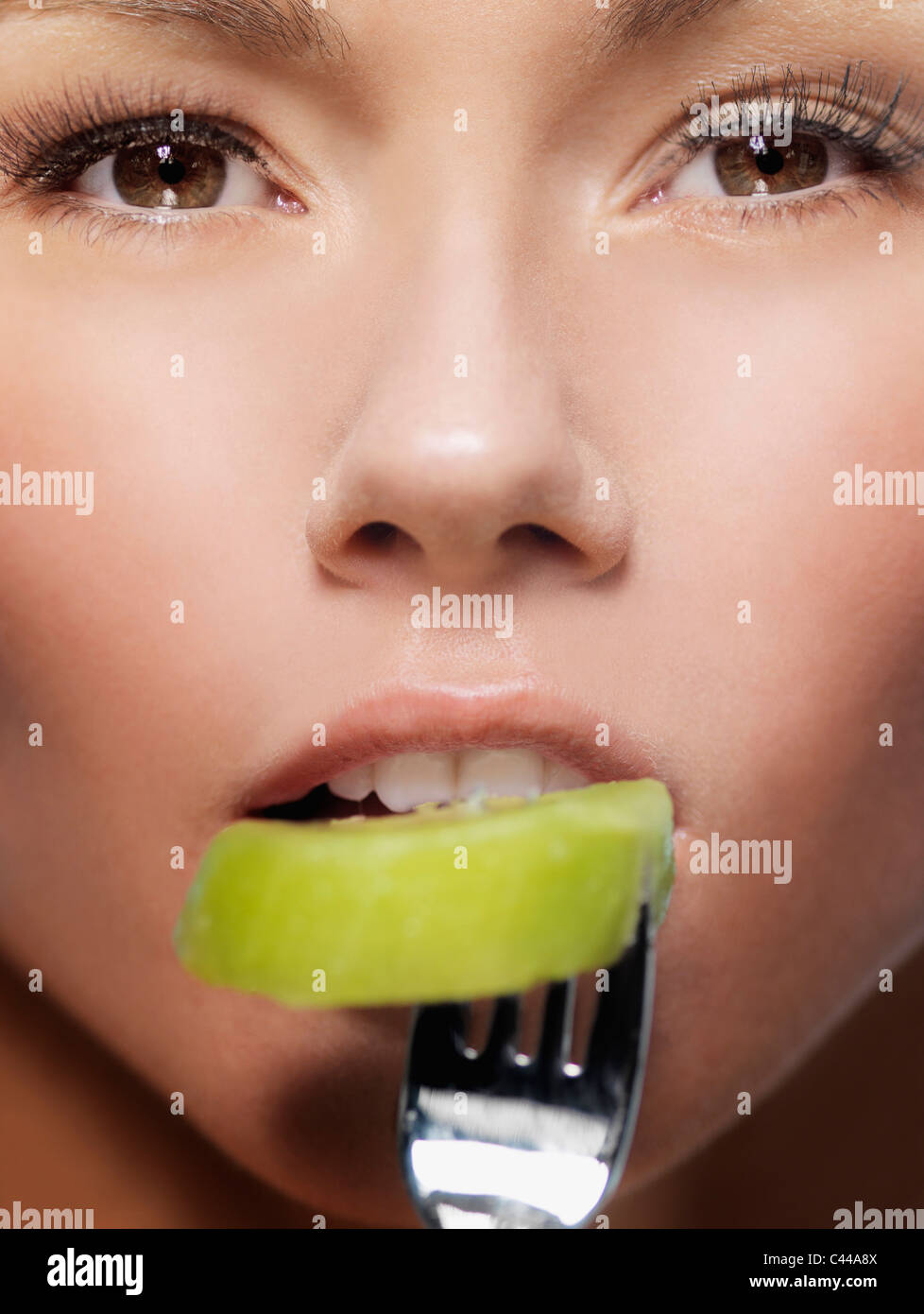 A woman biting a slice of kiwi on a fork, close-up of face Stock Photo