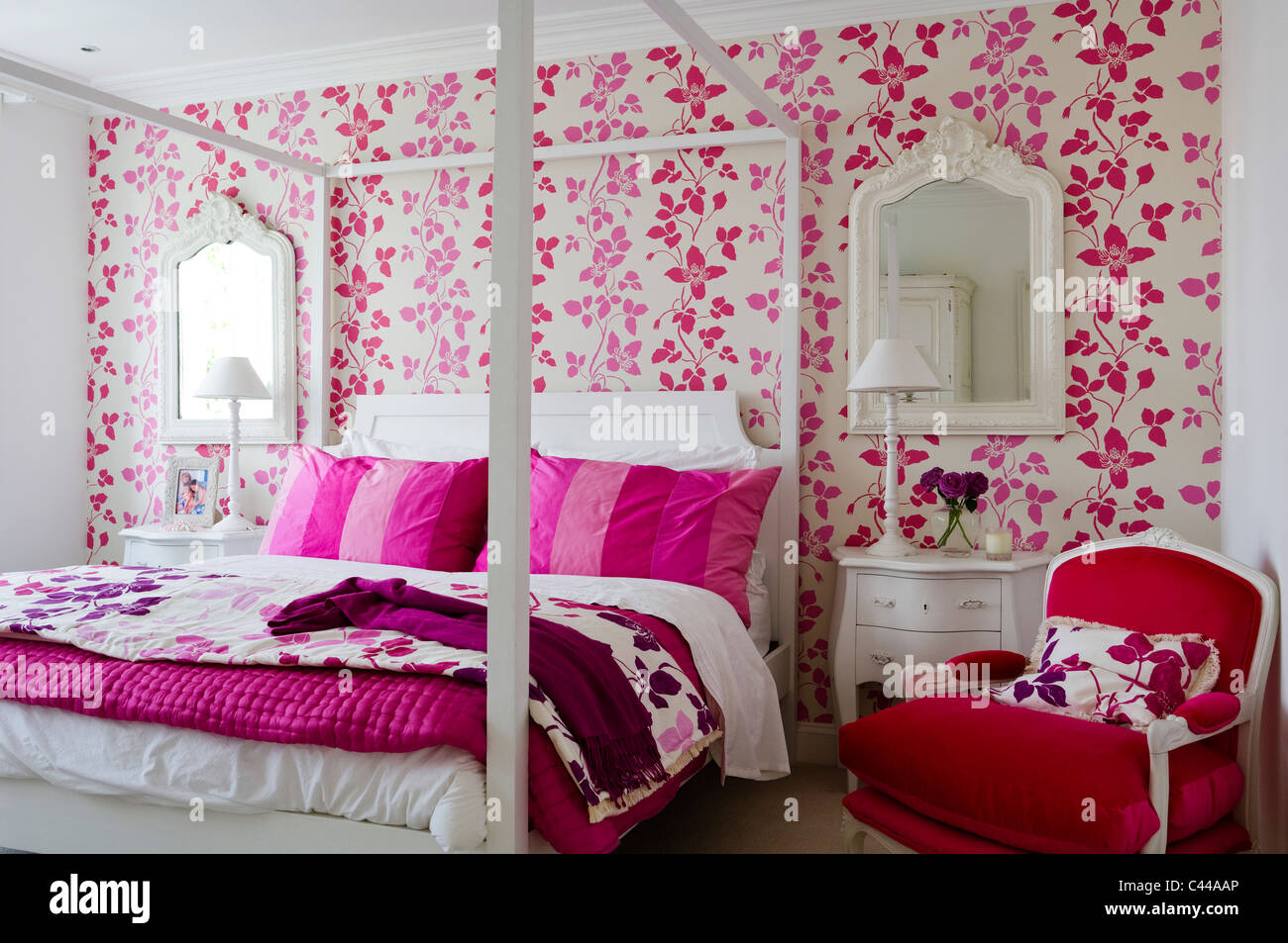Red velvet armchair in bedroom with fourposter bed and Designers Guild floral pink wallpaper Stock Photo