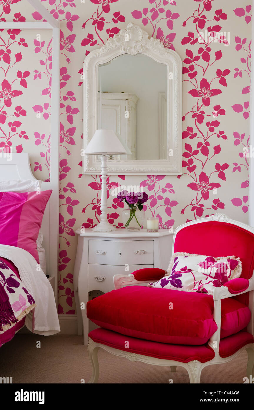 Red velvet armchair in bedroom with fourposter bed and Designers Guild floral pink wallpaper Stock Photo