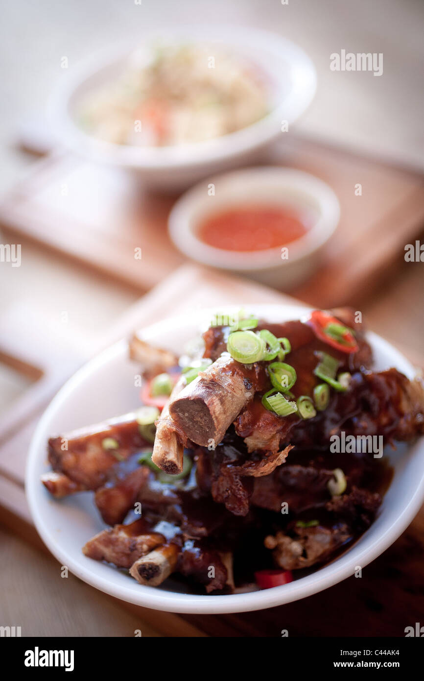 A dish of Chinese sticky pork ribs served with rice noodles and sweet chili dipping sauce, spring onions Stock Photo