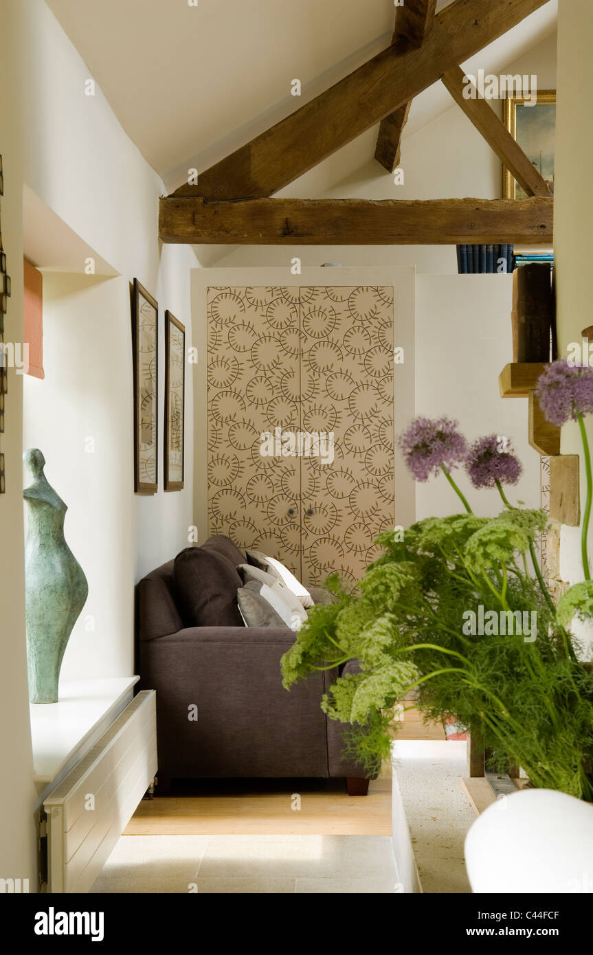 Flower arrangement in living room of converted barn with ceiling beams, sofa and patterned wallpaper cupboard Stock Photo