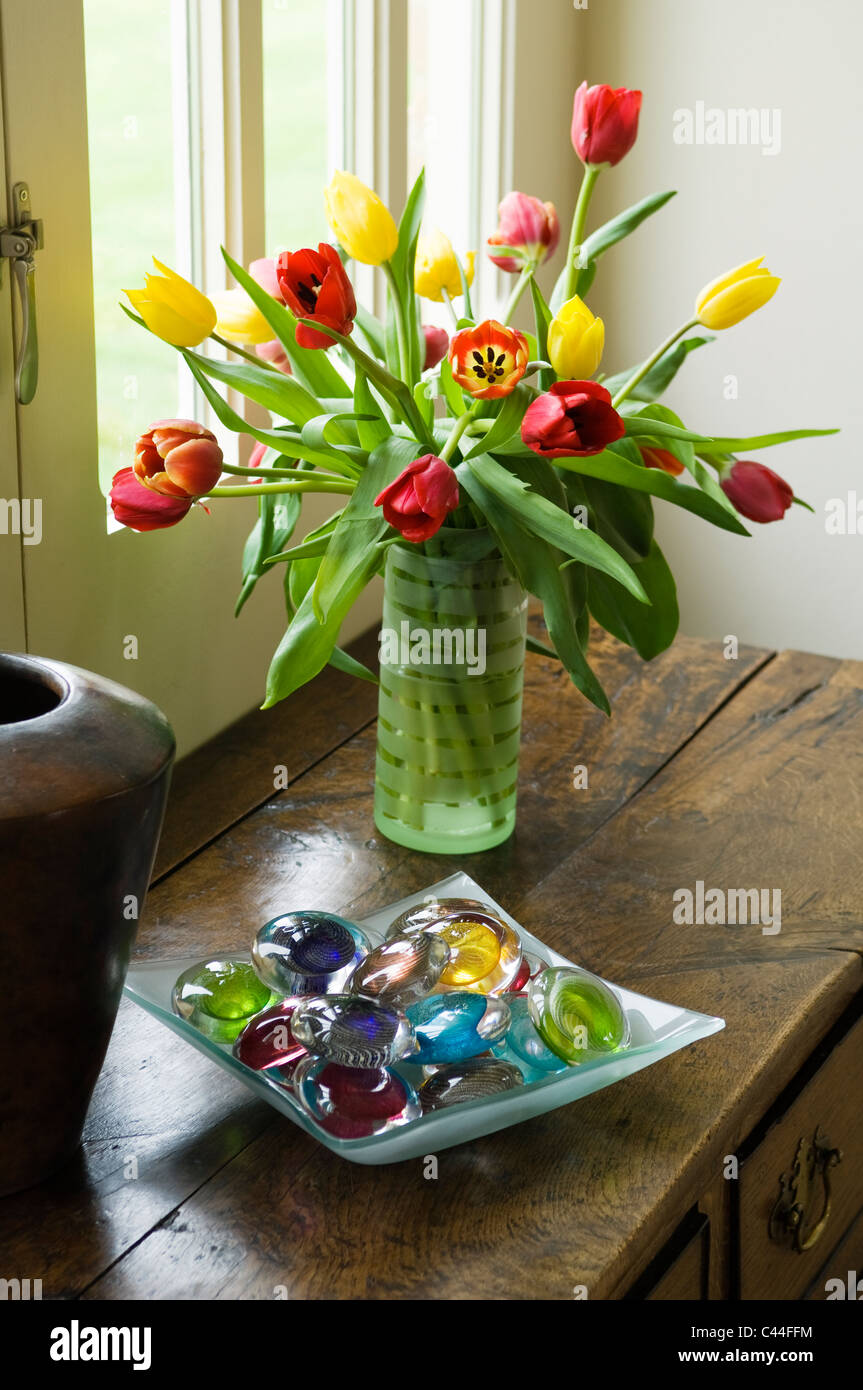 Vase of tulips on old wooden chest along with bowl of coloured glass pebbles Stock Photo