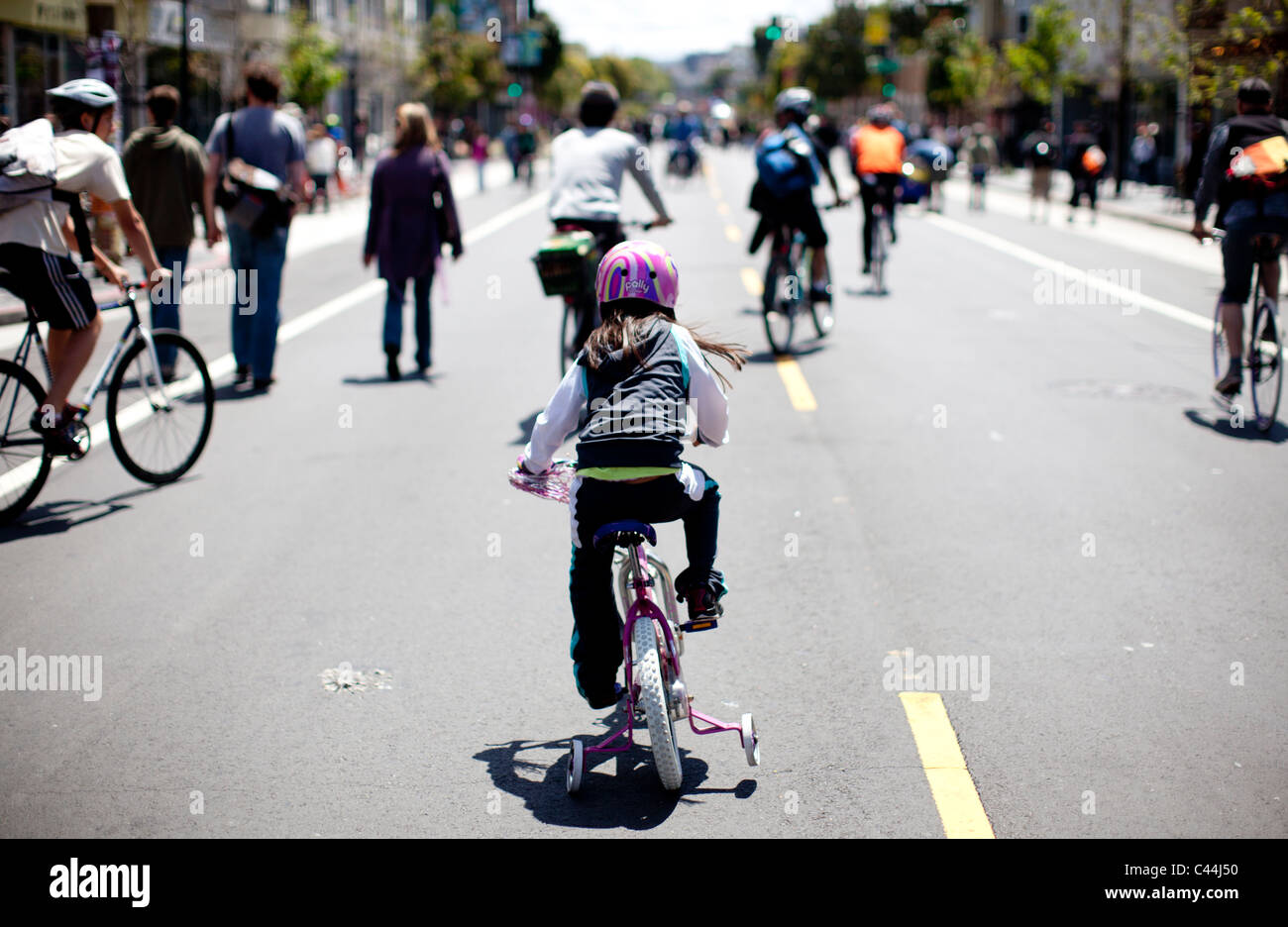 Girl cycles behind people on the street in San Francisco, California. Locals ride the closed streets once a month on a Sunday. Stock Photo