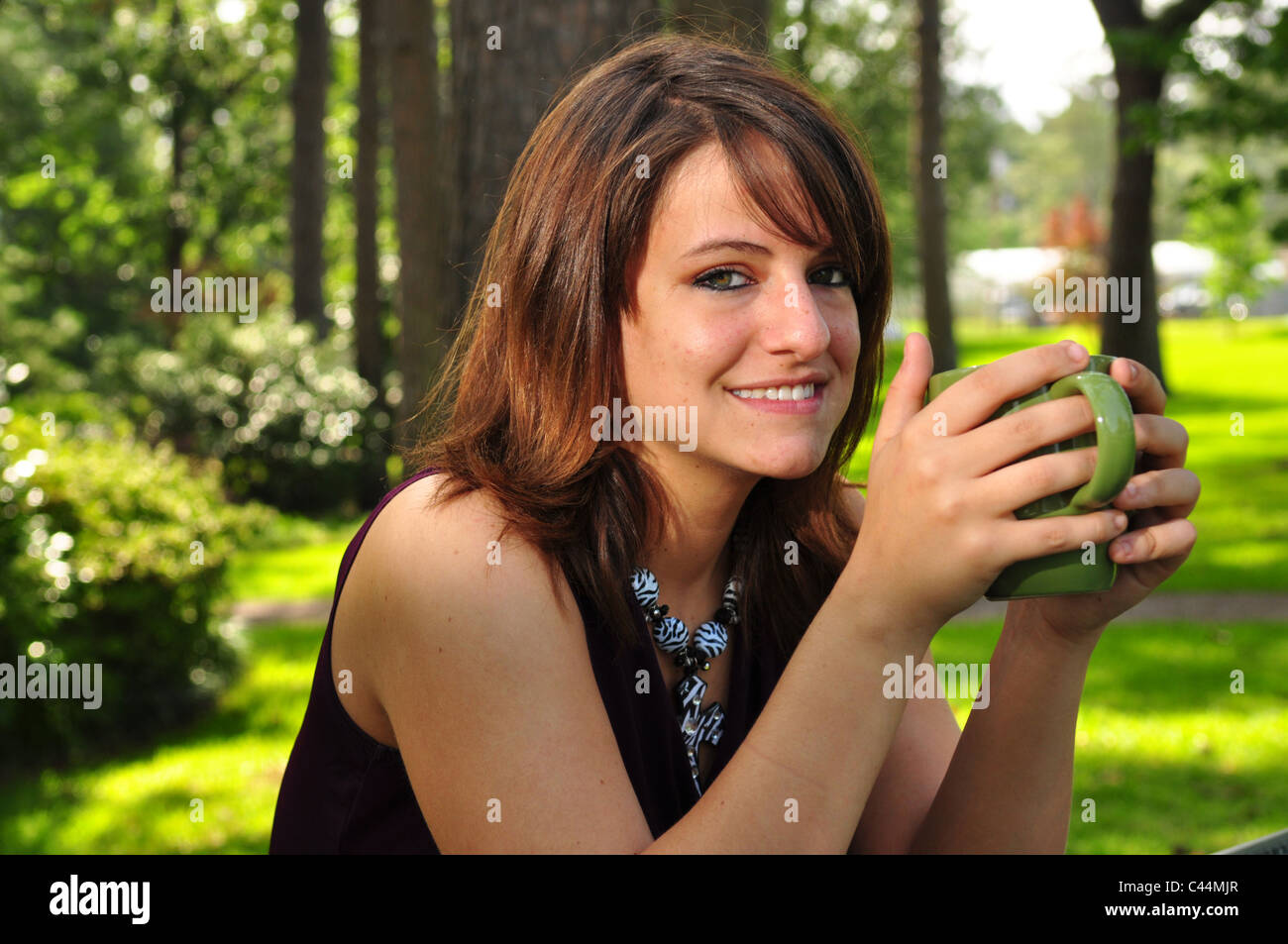 A pretty girl is sitting outdoors holding a coffee mug Stock Photo