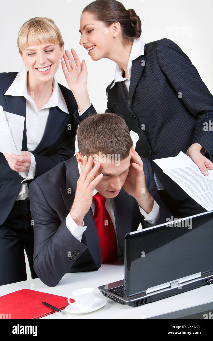 Photo of thinking boss in front of laptop while one of his employees whispering something to another woman Stock Photo