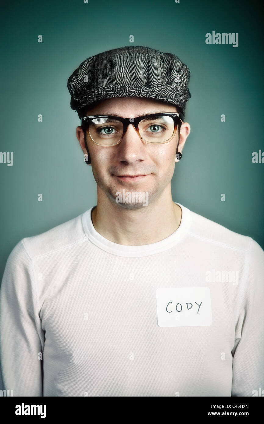 A hip yet friendly young man wearing a cap and plastic glasses with a name badge. He has an alternative look with gauged ears. Stock Photo