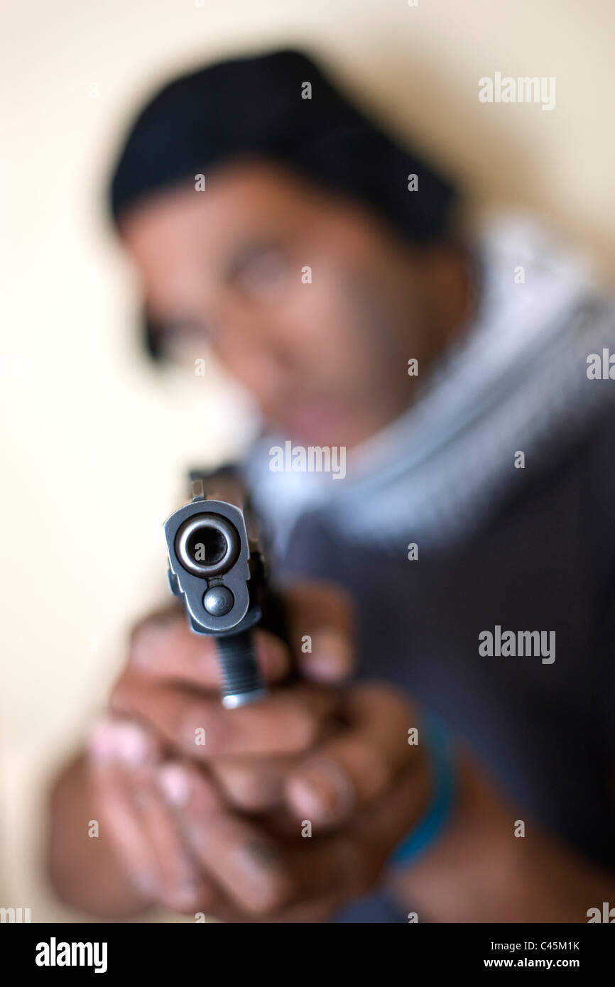 A man with a baseball cap pointing a pistol directly at camera. Stock Photo