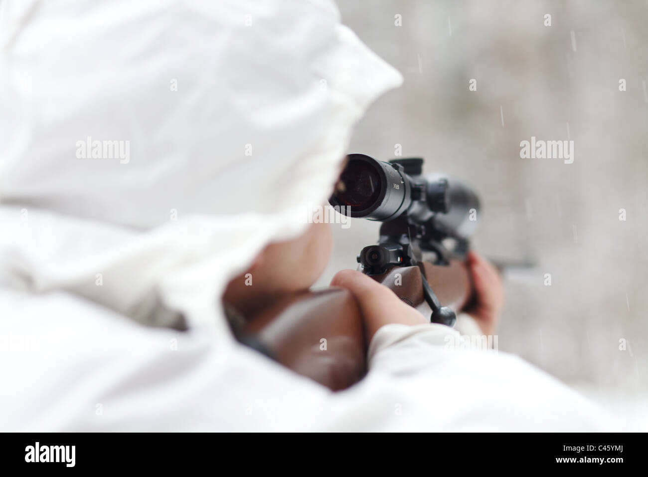 Soldier in white camouflage aiming with sniper rifle at winter forest. DOF Stock Photo