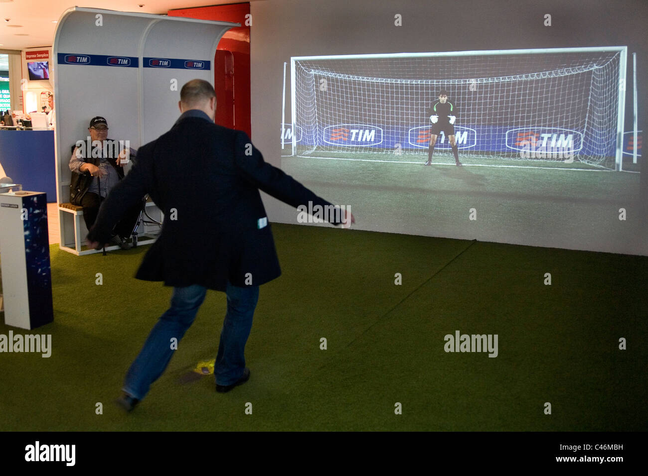 Man kicking a penalty with a virtual ball toward a projected goalkeeper and post at Fiumicino airport, Rome, Italy Stock Photo
