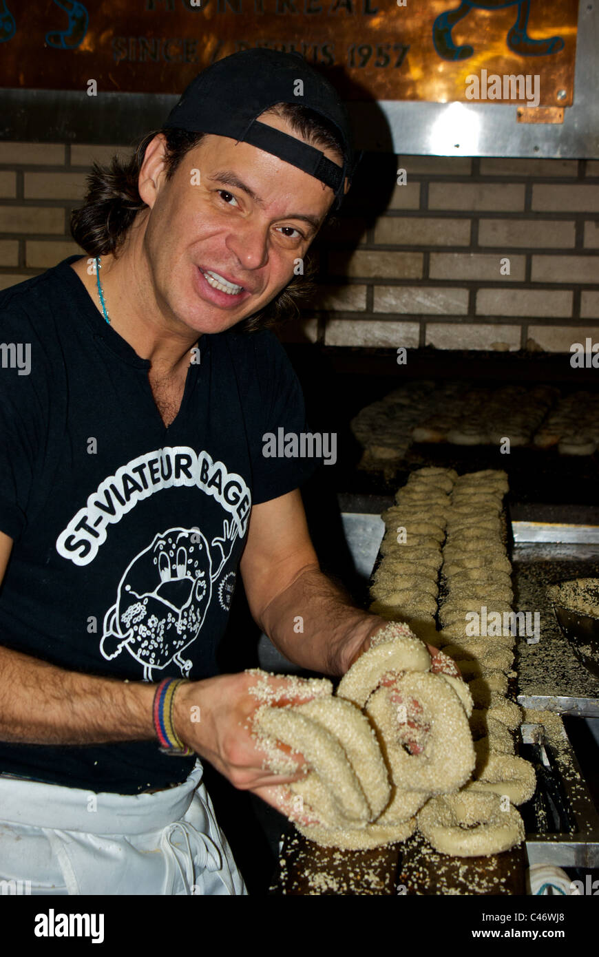 Baker coating hot boiled bagels in motion blur with sesame seeds before placing on wooden pallet for baking in wood-fired oven Stock Photo