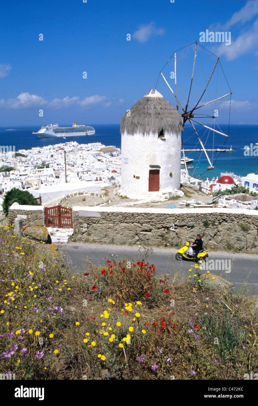 Man rides motor scooter  past windmill on mykonos island in Greece. Stock Photo