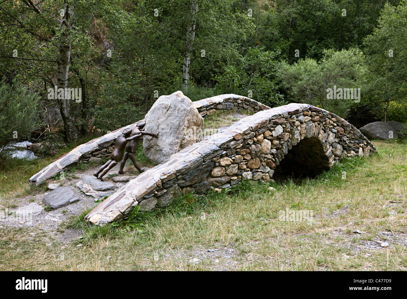 Statue of two people pushing large rock over a bridge Ruta del Ferro Llorts Andorra Stock Photo