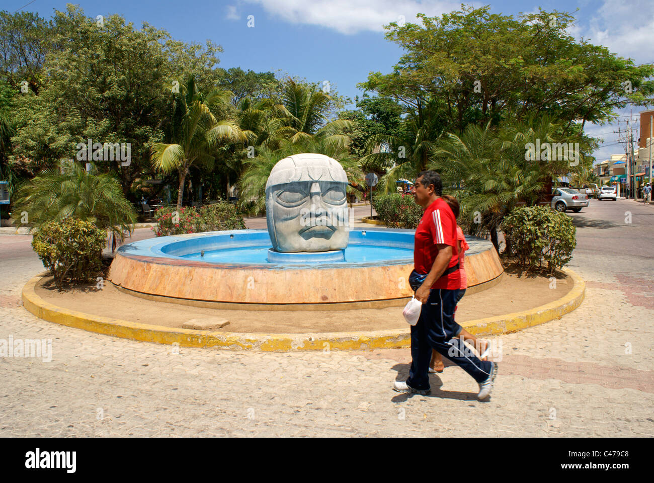 People walking past an Olmec stone head and fountain in Playa del Carmen, Riviera Maya, Quintana Roo, Mexico Stock Photo