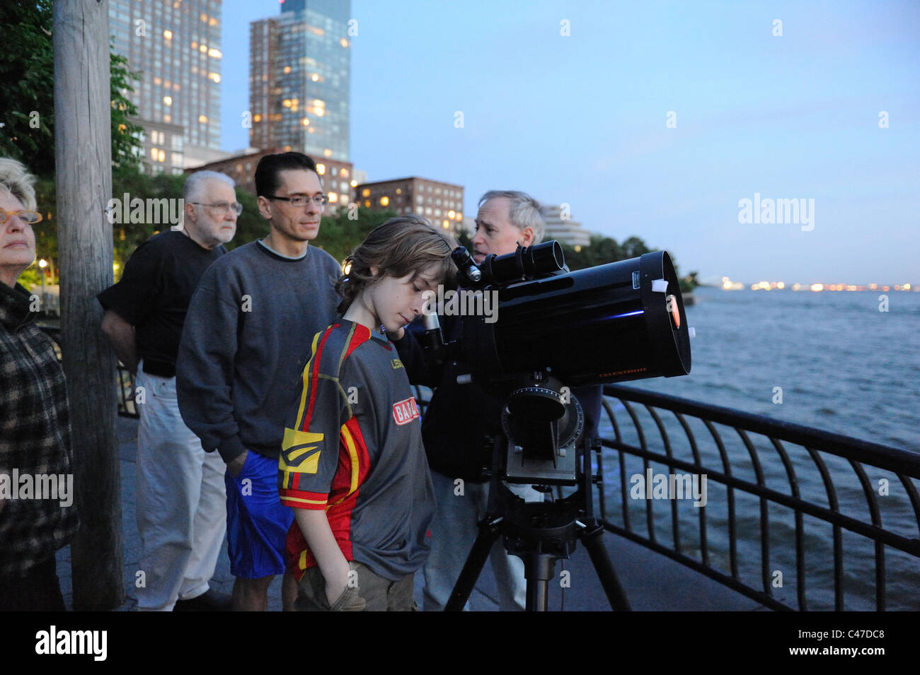 People looked through a telescope at the moon and Saturn from the shore of the Hudson River in Manhattan's Battery Park City. Stock Photo