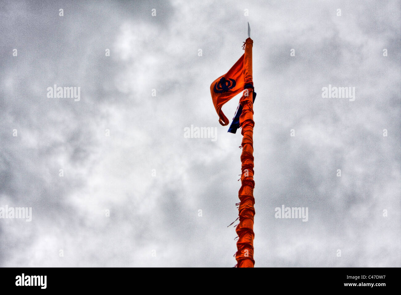 The Sikh flag is a saffron-coloured triangular-shaped cloth, usually reinforced in the middle with Sikh insignia in blue. Stock Photo