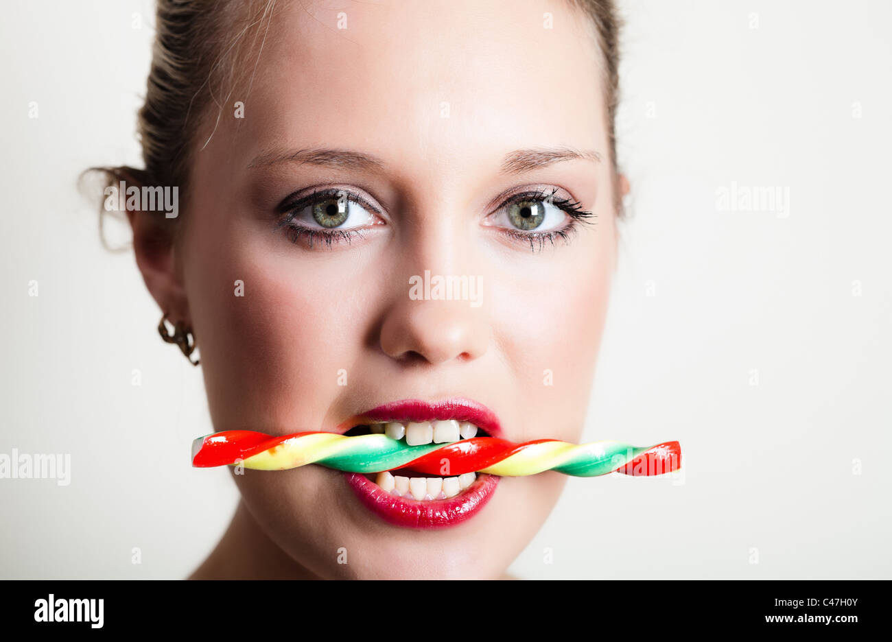 Portrait of young woman holding colorful candy in her teeth Stock Photo