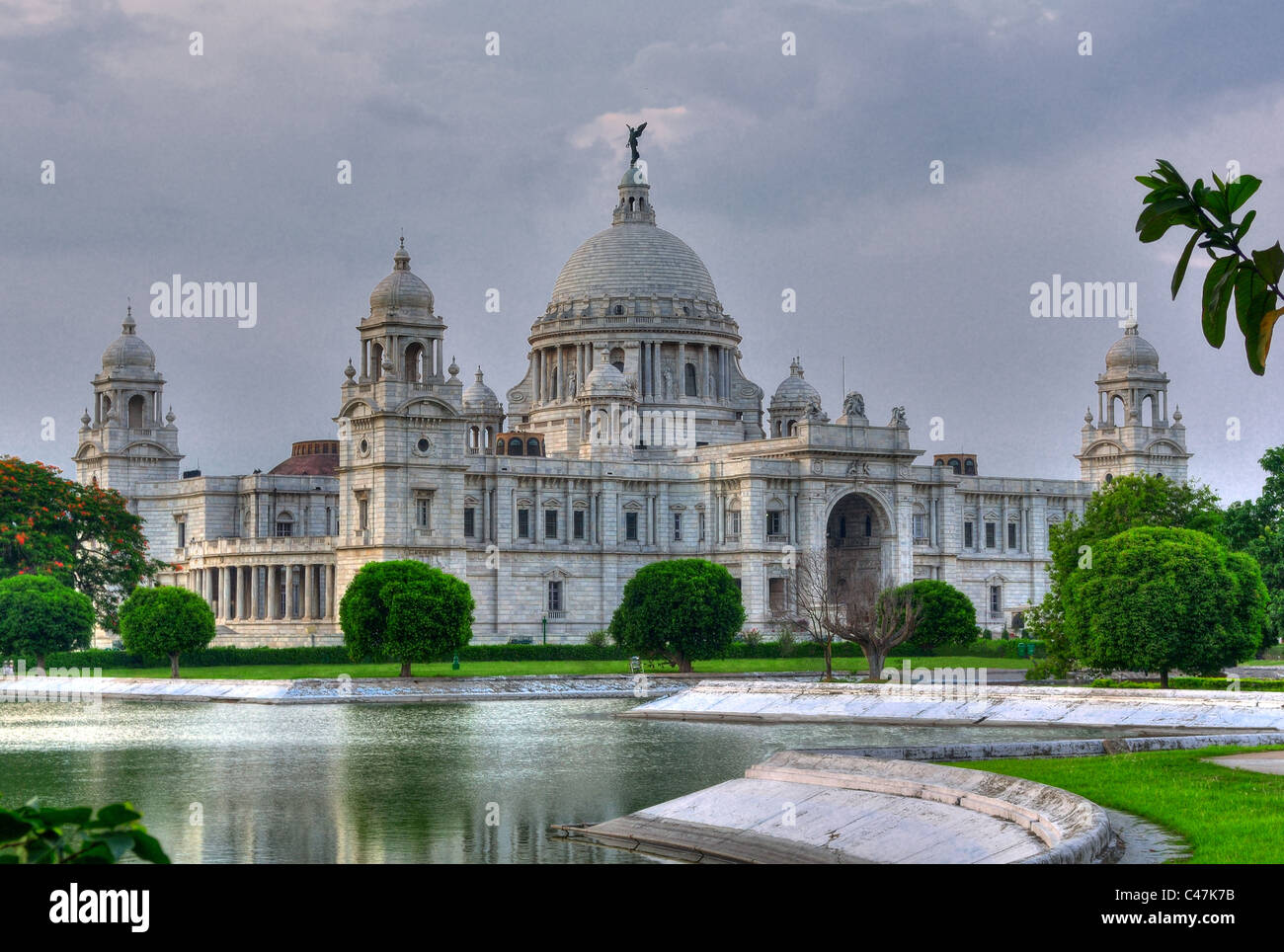 Victoria Memorial Hall, Calcutta, Kolkata in evening light showing Queen's Garden in foreground with green grass, trees and pond Stock Photo
