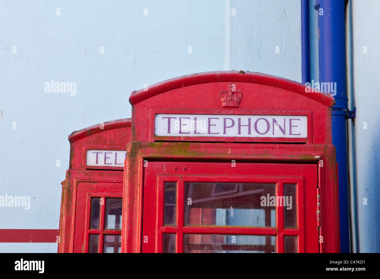 Tops of 2 iconic british red telephone boxes against a blue wall in St Ives, Cornwall Stock Photo