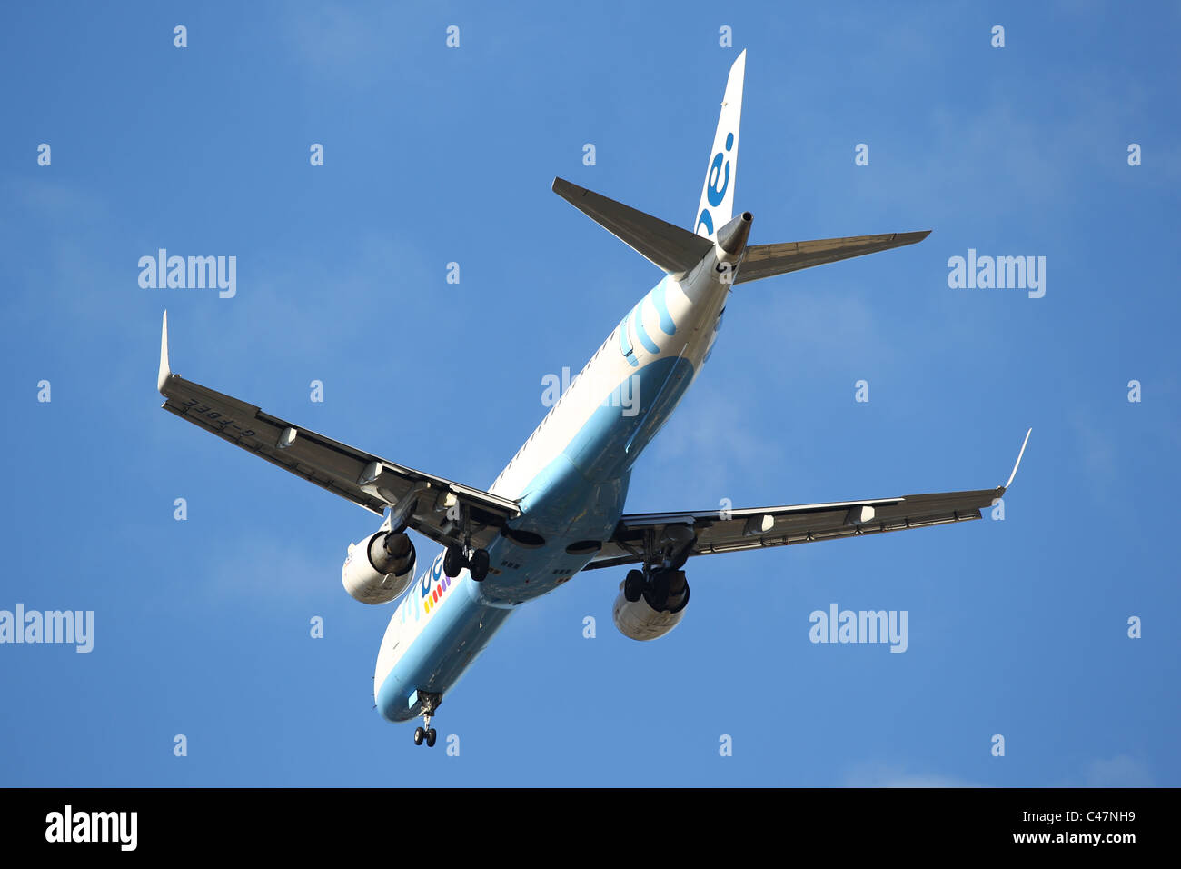Jet Aeroplane flying over head coming in to land against a blue sky - Fly be Stock Photo