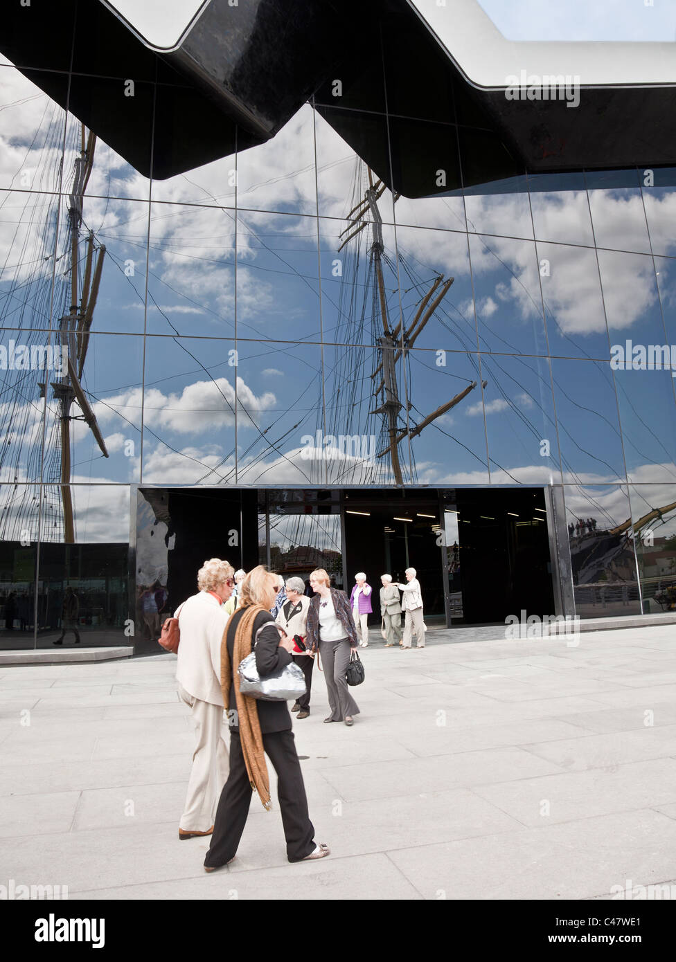 Visitors outside the Riverside Museum, Glasgow. The masts of the Glenlee (Tall Ship) are reflected in the glass wall. Stock Photo