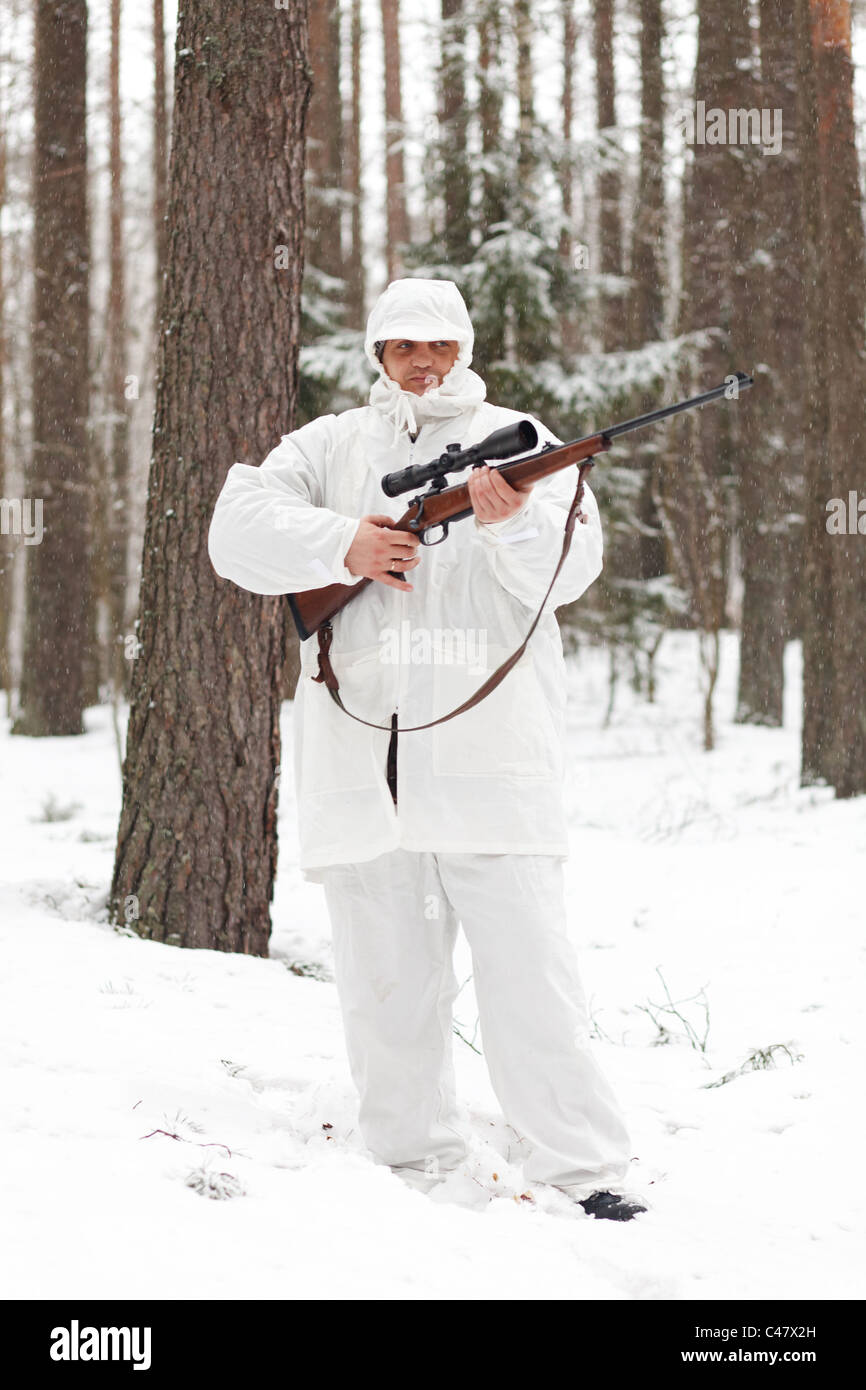 Sniper in white camouflage  with rifle at winter forest. Stock Photo