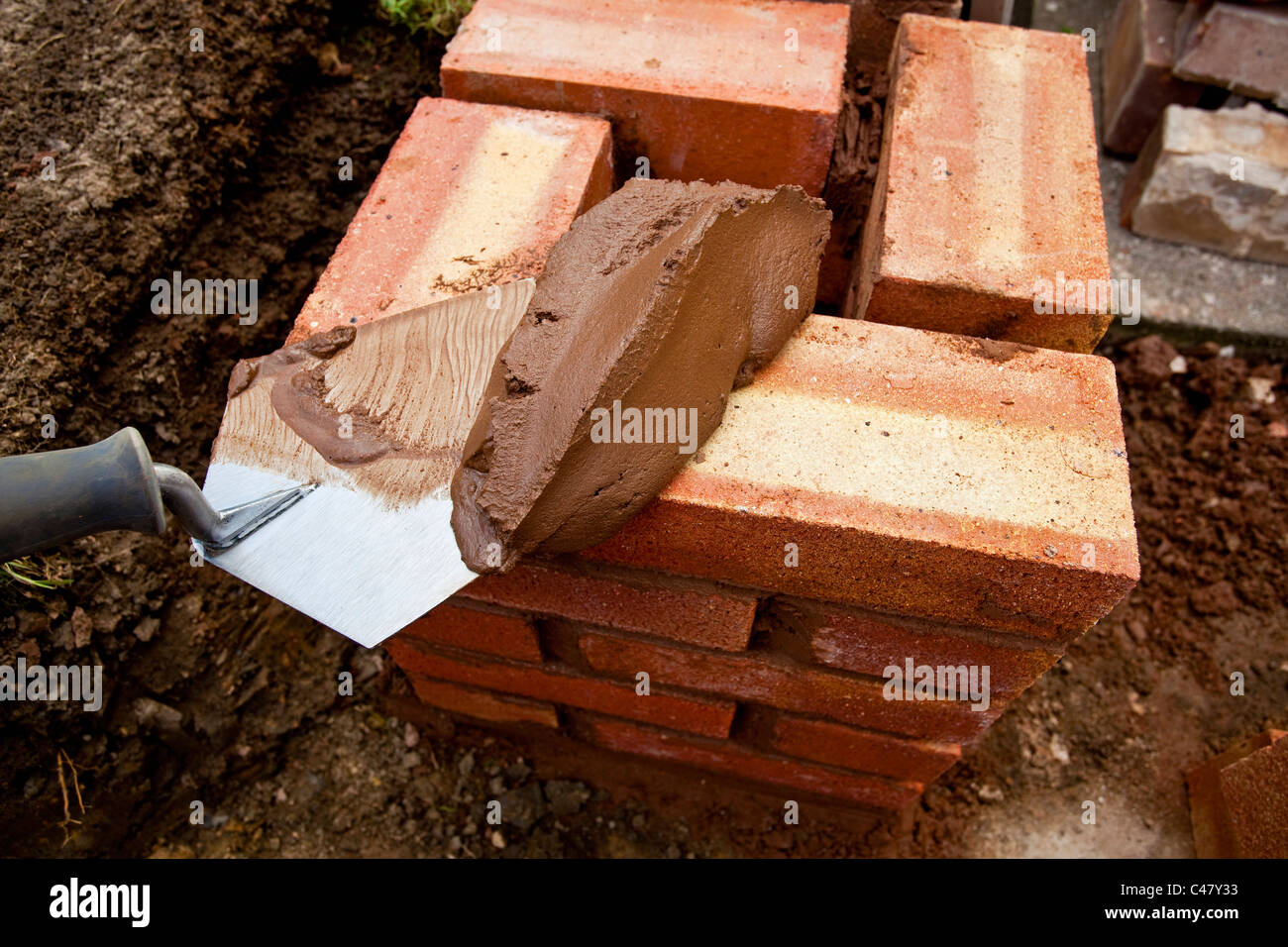 A trowel of building mortar on top of a new wall of bricks uk Stock Photo
