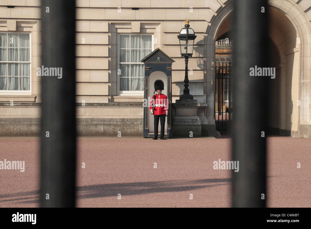A view through the railings outside Buckingham Palace, London, UK. of a soldier of the Queen's Guard on duty. Stock Photo