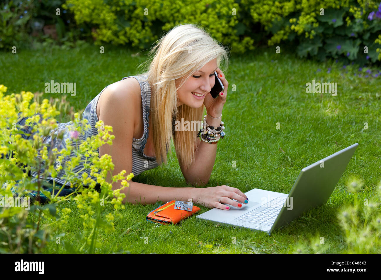 Young girl on moblie phone while on the internet, chatting and socializing on wireless laptop computer in the garden Stock Photo