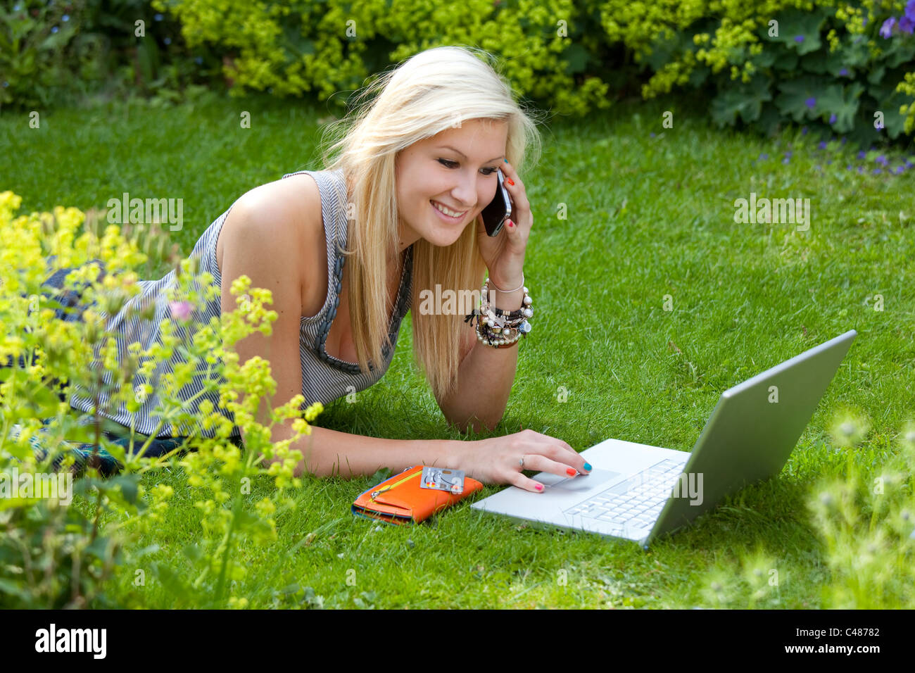 young girl on moblie phone while on the internet, chatting and socializing on wireless laptop computer in the garden Stock Photo