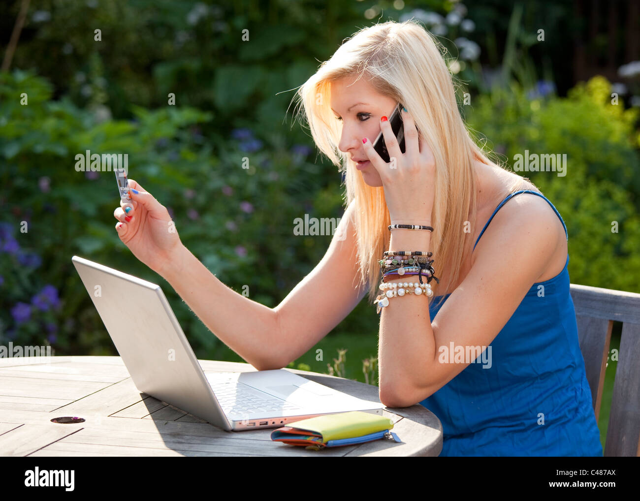 Young girl talking on moblie phone online shopping with credit card in the garden on a wireless laptop computer Stock Photo